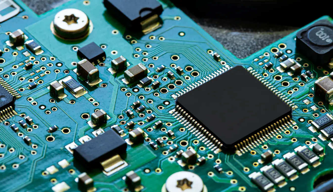 Close-up view of a green printed circuit board featuring an integrated black microchip and various electronic components.