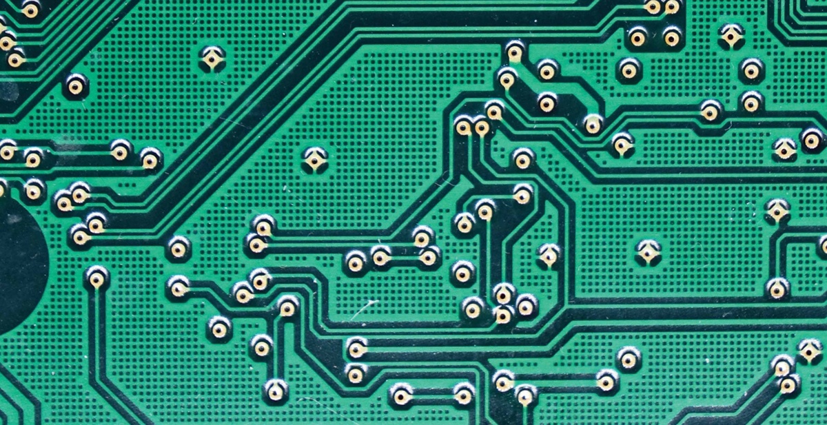 Close-up of a green printed circuit board showing intricate patterns of electrical pathways and numerous solder points.
